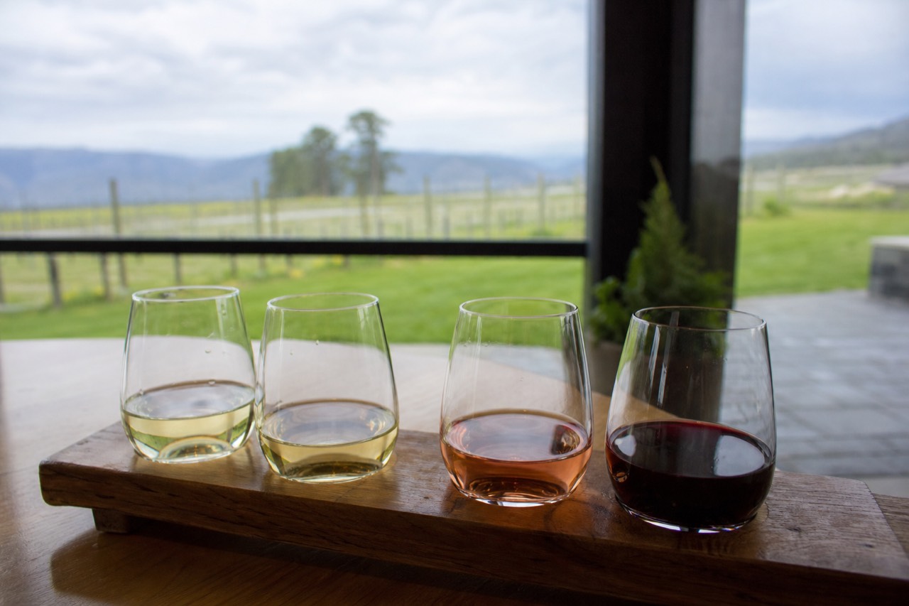 Four small tasting pours lined up on a wooden flight board with vineyard light behind, no people, no logos.