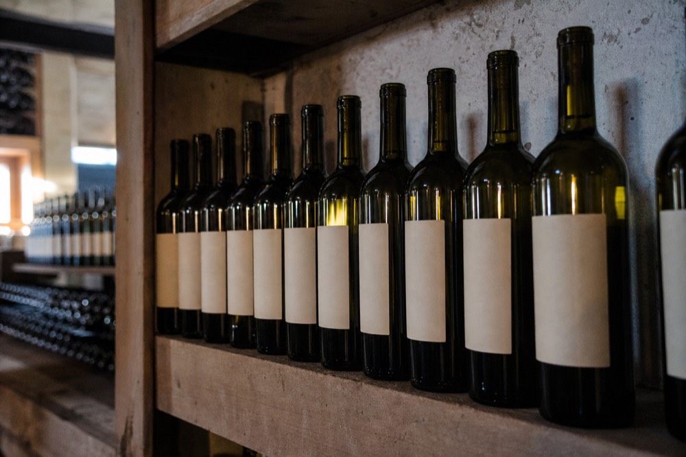 A row of wine bottles on a cellar shelf with blank labels, soft light, no readable text, no branding, no people.